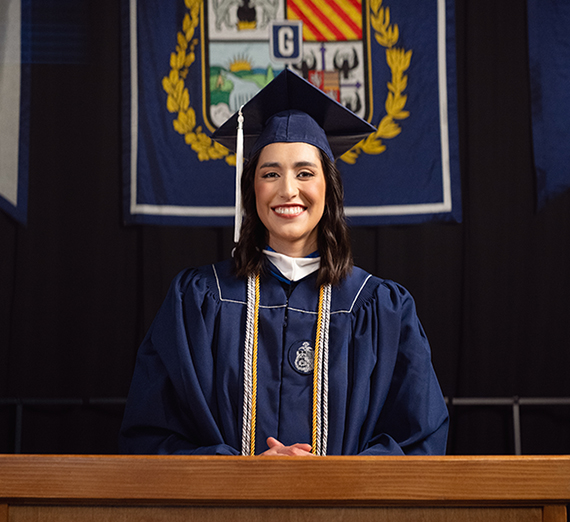 A woman in graduation cap and gown smiles at the camera