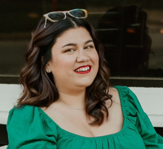 Woman with brown hair, sunglasses on head and wearing green shirt with a dark background