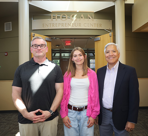 Two men and a woman stand in front of a sign for Hogan Entrepreneur Center