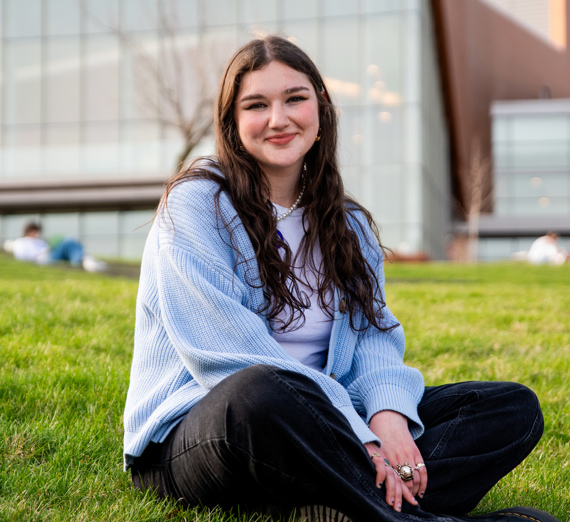 Senior Sydney Baltuck sitting cross legged outside the Myrtle Woldson Performing Arts Center.