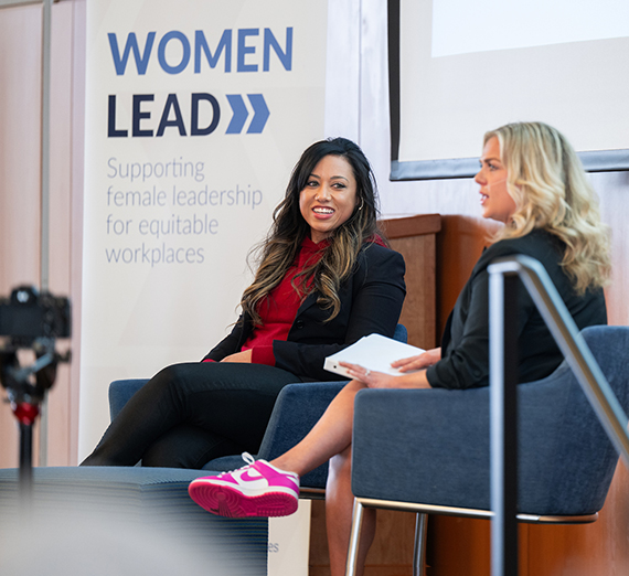 Mandi Price and Morgan Marie sit on a stage in front of a sign that says Women Lead