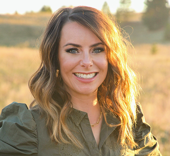 Sarah Gore wearing green shirt and standing outside with a field and hills in the background