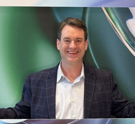 MBA Alumnus, Erik Snyder, male with short brown hair wearing white button up and navy blazer in front of a colorful background.