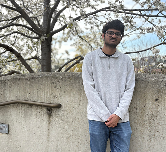 Man leans against brick wall with cherry blossom tree behind it.