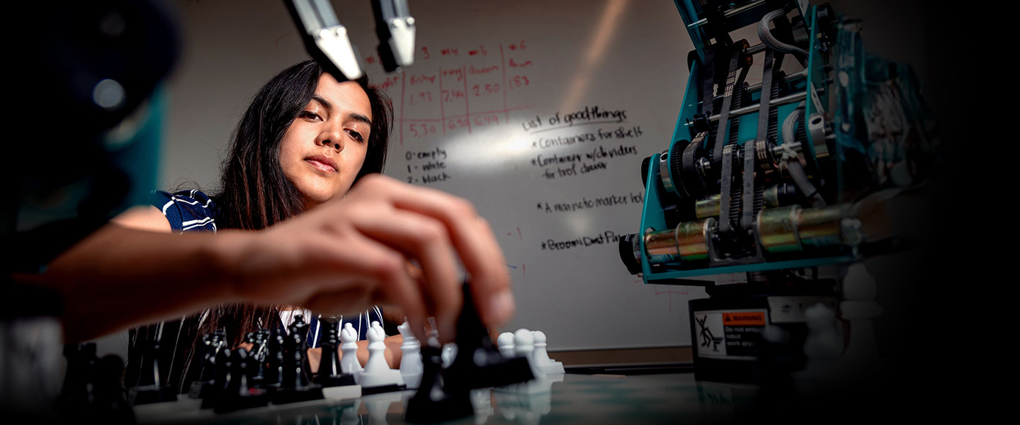 A student playing chess with a robot as the competitor in a classroom.