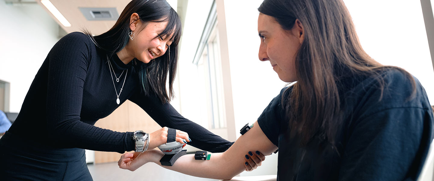 woman applies medical device to another woman's arm