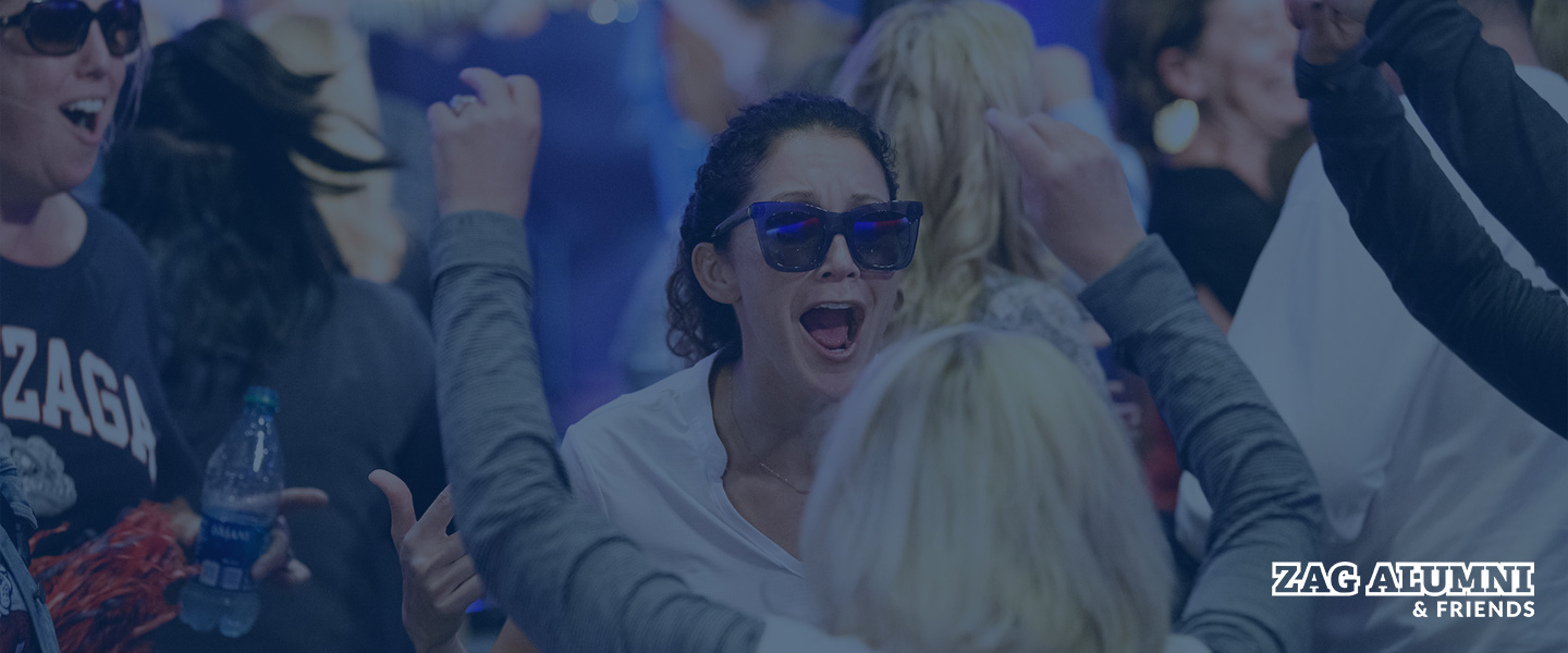 Alumni excitingly  embrace at an event with the Alumni & Friends logo in the bottom right